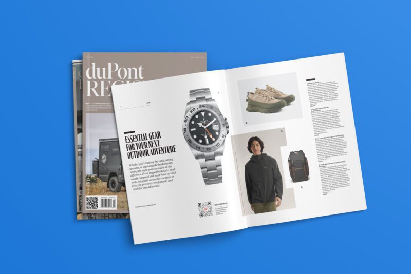 Open magazine from the duPont REGISTRY, May 2025, No. 480 edition displays outdoor gear, including a watch, shoes, a backpack, and a man modeling clothing. The background showcases a blue surface alongside a stack of two additional magazines.