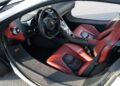 Interior of a modern sports car featuring red leather seats, a sleek dashboard, and a central control panel; driver’s door is open.