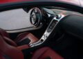 Interior view of a luxury sports car featuring red leather seats, a modern dashboard, a central touchscreen display, and a sporty steering wheel.