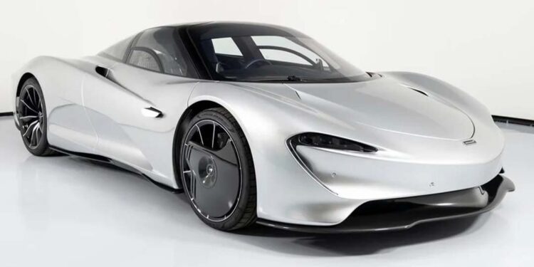 A silver McLaren Speedtail hypercar, inspired by the Electrified Longtail concept, is parked in a white studio, featuring a sleek, aerodynamic design with black accents and futuristic wheels.