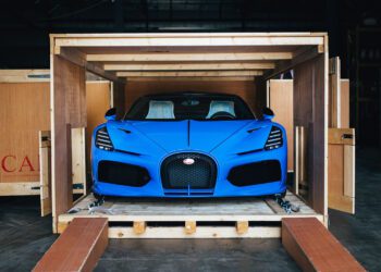 A Bugatti Mistral in striking French Racing Blue sits poised inside a wooden shipping crate, with its sleek front facing outward.
