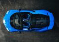 Aerial view of a sleek Bugatti in French Racing Blue with an open roof, showcasing its Mistral design, two seats, and a detailed engine compartment against a dark background.