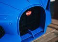 A close-up of a Bugatti Mistral car grille in classic French Racing Blue, adorned with the iconic red Bugatti emblem at its center. The design showcases sleek lines and a stylish mesh pattern, perfectly capturing the elegance associated with Miller Motorcars.
