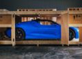 A sleek Bugatti Mistral in French Racing Blue is partially exposed, nestled inside a wooden shipping crate labeled "FRAGILE," its impressive 600HP engine waiting to unleash its power.