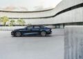 A dark blue sedan is parked in an empty, modern concrete courtyard with curved architectural walls and palm trees in the background.