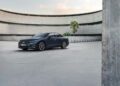 A dark blue Audi New A6 sedan is parked on a wide concrete surface in front of a curved, modern building with palm trees.