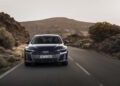 A black Audi A6 sedan drives on an empty road through a rocky, mountainous landscape under a clear sky, capturing the thrill of the new Audi sedan.