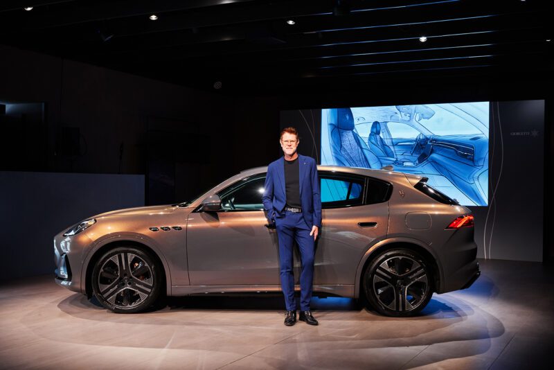 A person stands beside a silver luxury Maserati SUV in a showroom, where a display highlights the vehicle's elegant interior, evoking the sophistication of Milan Design Week.