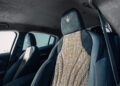 Car interior with two front seats featuring a mix of textured fabric and smooth upholstery, crafted with a nod to Milan Design Week. The headrests proudly display Maserati's trident logo. In the background, a blurred car door and window subtly underscore the luxurious design theme.
