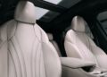 Front view of two white leather car seats with Maserati logo embossed on headrests in the 2025 Grecale, panoramic sunroof above, and part of the center console in foreground.