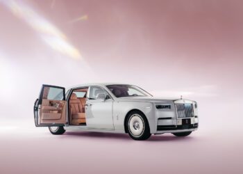 Luxury car with a white exterior, open passenger door, and tan leather interior, displayed against a soft pink background.