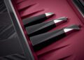 Three sleek, black and silver, geometric kitchen utensils are displayed on a red surface next to a dark marbled countertop, evoking the craftsmanship of a bespoke chess set.