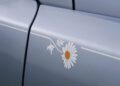 Close-up of a silver Rolls-Royce car door featuring a Cullinan Daisy decal with a yellow center and a white stripe along the side.