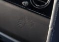 Close-up of a Rolls-Royce Daisy dashboard with an embossed flower next to a round air vent and part of a stitched leather seat.