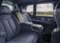 The image shows the luxurious rear passenger seats inside a Rolls-Royce Cullinan, featuring leather upholstery, a central armrest, and a window view of a grassy landscape.