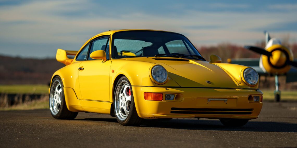 A yellow Porsche 911 Turbo gleams on the tarmac, poised beside a sleek airplane under the expansive blue sky—a scene that echoes the elegance often celebrated at Broad Arrow Auctions.