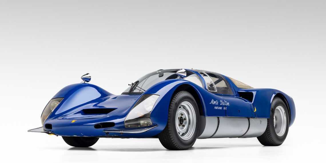 A sleek blue vintage racing car with aerodynamic curves, silver accents, and prominent front air intakes, reminiscent of the iconic 1966 Porsche 906, sits elegantly in a studio setting. Perfect for any collector anticipating the next Broad Arrow Auctions event.