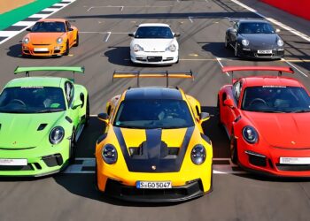 Six Porsche sports cars, including the iconic Porsche 911 GT3 RS in vibrant colors, are parked on a racetrack in two neat rows, all facing forward.