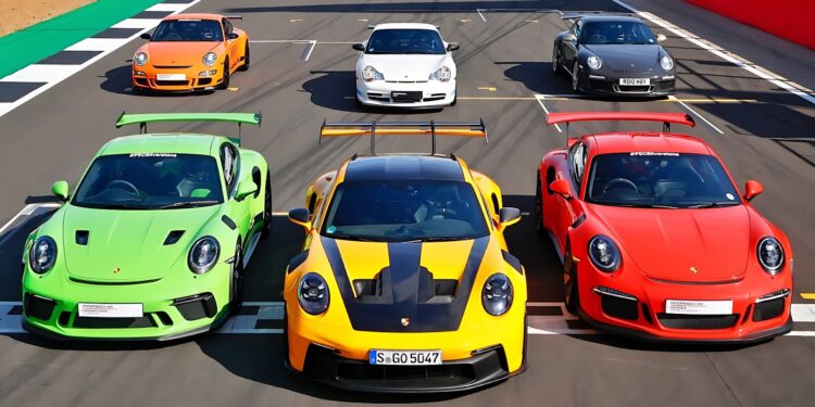 Six Porsche sports cars, including the iconic Porsche 911 GT3 RS in vibrant colors, are parked on a racetrack in two neat rows, all facing forward.