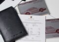 Black Porsche-branded folder, two Porsche 959 Speedster manuals, and a printed document are displayed on a flat surface, as seen at RM Sotheby’s Milan auction.