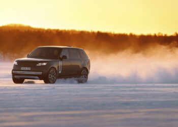 A black Range Rover Electric drives across a snow-covered landscape in Sweden at sunset, kicking up a cloud of snow behind it during cold weather testing.