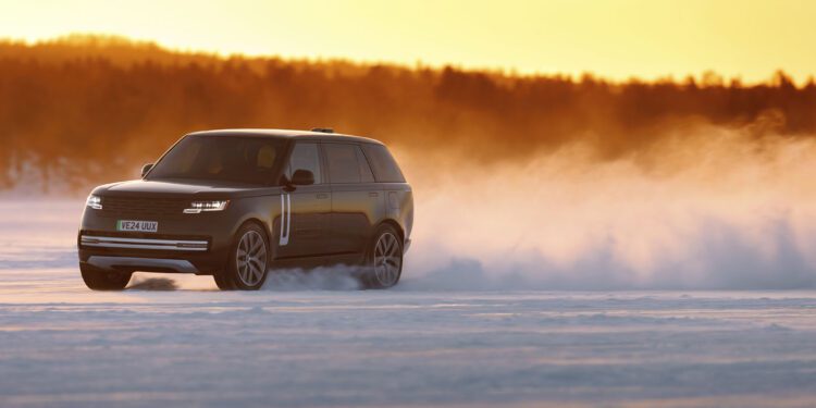 A black Range Rover Electric drives across a snow-covered landscape in Sweden at sunset, kicking up a cloud of snow behind it during cold weather testing.