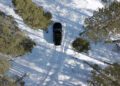 A black Range Rover Electric is parked on a snowy path in a forest, surrounded by tall green pine trees, as seen from above—perfect for cold weather testing in Sweden.
