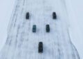 Five black SUVs, likely Range Rover Electric models, are driving on a wide, snow-covered and icy road in Sweden, undergoing cold weather testing as seen from above.