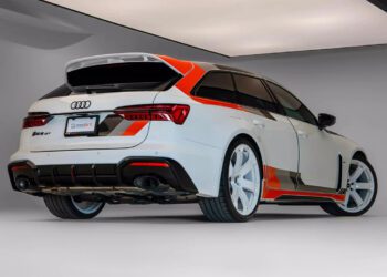 A white Audi RS 6 Avant, a high-performance wagon from Germany with red and black accents, large white wheels, and a sporty body kit is parked indoors under bright lighting.