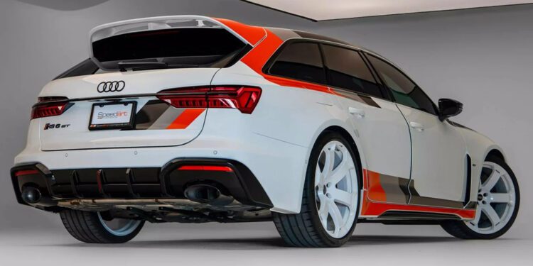 A white Audi RS 6 Avant, a high-performance wagon from Germany with red and black accents, large white wheels, and a sporty body kit is parked indoors under bright lighting.