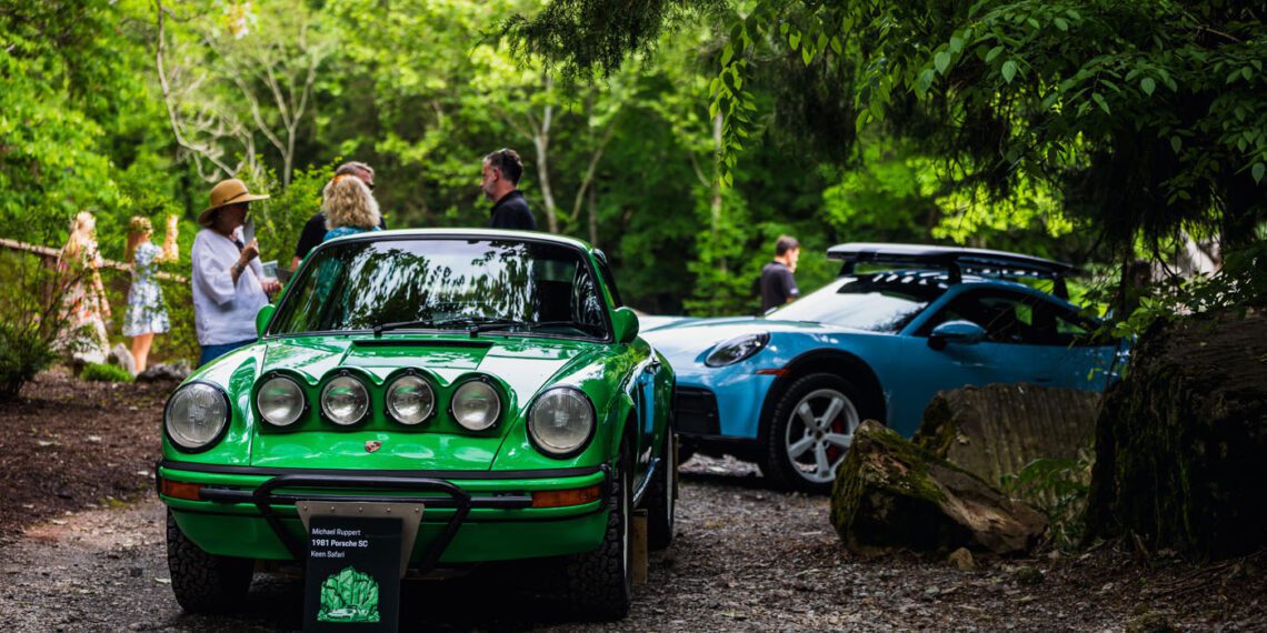 A green vintage Porsche sits elegantly outdoors beside a sleek blue sports car, drawing admirers into animated plática amid the shade of towering trees at this vibrant event.