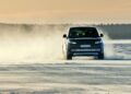 A black Range Rover Electric drives across a snowy, frozen landscape, kicking up snow as it moves forward under a cloudy sky, showcasing its impressive 300 mile range.