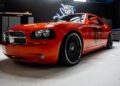 A bright orange Dodge Charger with black custom wheels, styled by West Coast Customs and featuring the number "01" on the door, parked indoors in a garage setting.