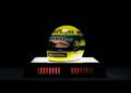 A racing helmet displayed on a lit platform evokes the legacy of Ayrton Senna. Primarily yellow with green and blue stripes, it features logos for "John Player," "Renault," and "Nacional," capturing the essence of F1 victory.
