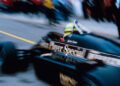 A blurred image captures the iconic Lotus Formula 1 car in motion, bearing the "John Player Special" branding as it speeds down the track, reminiscent of Ayrton Senna's legendary prowess.