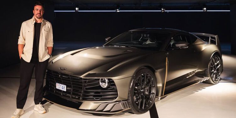In a dimly lit showroom, a man stands beside a sleek, dark Aston Martin sports car, its unique grille and angular design echoing the elegance of Monaco's streets.