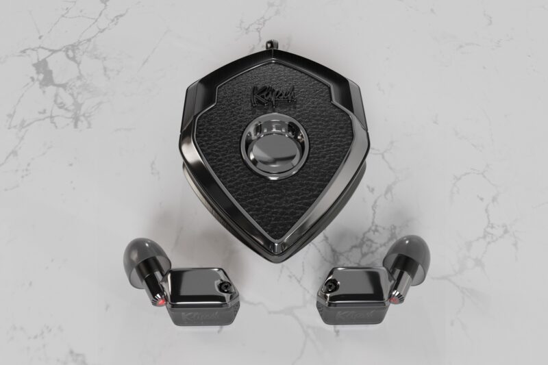 A pair of black wireless earbuds with a matching shield-shaped charging case—perfect luxury accessories—are displayed on a white marble surface.