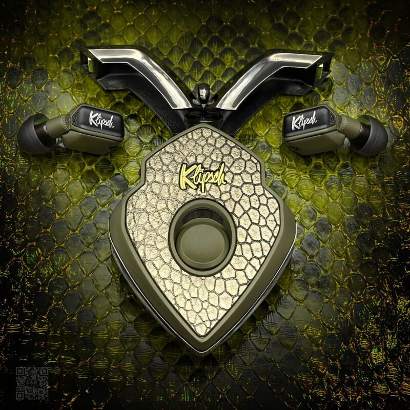 Three Klipsch audio devices are arranged on a textured, reptile-patterned surface to resemble a stylized animal face. The central speaker displays the Klipsch logo—perfect luxury accessories to upgrade your style and sound experience.