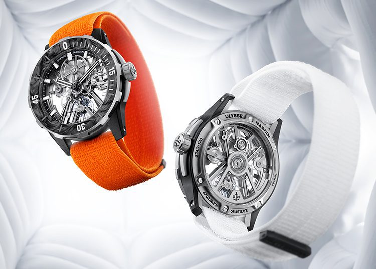 Two wristwatches with transparent cases reveal their intricate Ulysses Nardin mechanisms; one sports an orange band, the other a white band, set against a white, quilted background. Perfect for the Watches & Wonders enthusiast seeking unique craftsmanship.