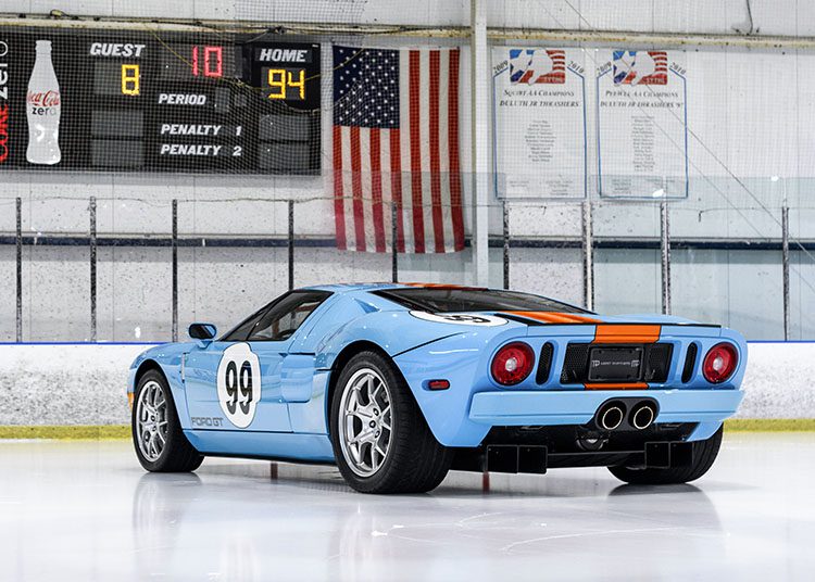 A blue Ford GT Heritage Edition with number 99 on its side is parked on an ice hockey rink. The scoreboard shows the home team with 94 points and the guest with 8. An American flag hangs on the wall, reminiscent of Wayne Gretzky's legendary days on ice.
