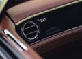 Close-up of a Bentley dashboard with Heritage Leather Interior in brown, featuring a circular air vent and the word "Mulliner" with a car outline logo on a sleek black panel.