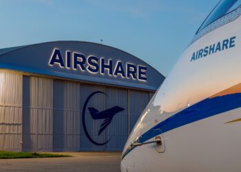 Aircraft parked outside an Airshare hangar at dusk, with the hangar logo illuminated. The plane's nose peeks into view, embodying a perfect fit against the evening sky, ready to fly.