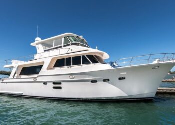 A white luxury yacht is docked at a marina on a sunny day, offering a true maritime experience with clear blue sky and calm water surrounding the boat.