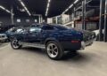 A classic black Ford Mustang fastback, a true icon among classic muscle cars, is parked indoors in a well-lit garage with other cars visible in the background.