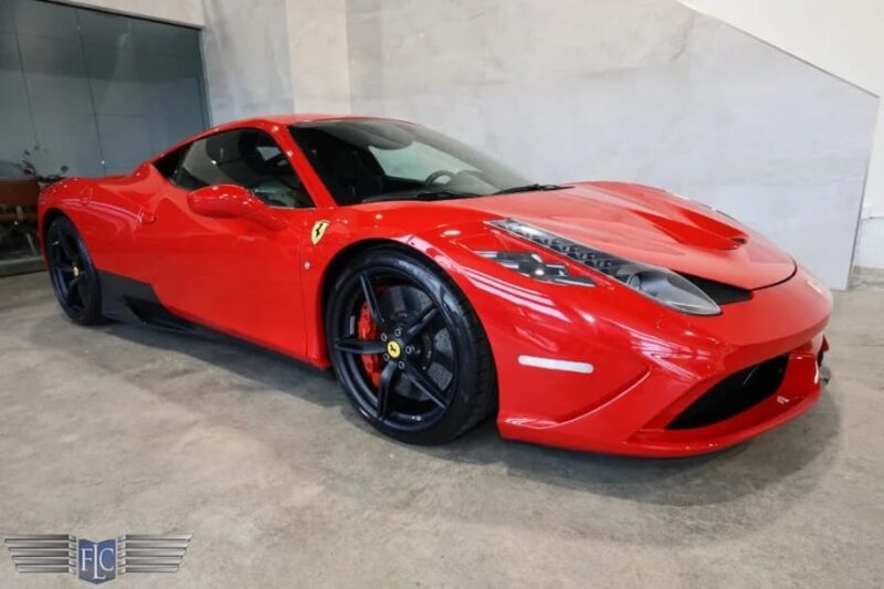 A red Ferrari luxury car is parked indoors on a concrete floor, viewed from the front left side.