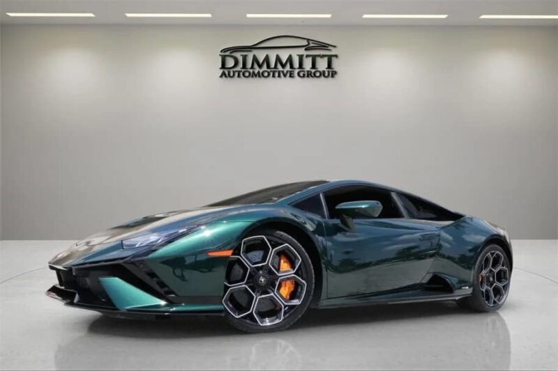 A dark green Lamborghini sports car with orange brake calipers is displayed indoors under bright lighting, with the Dimmitt Automotive Group logo on the wall behind—an exceptional exotic car for sale featured in top car listings.