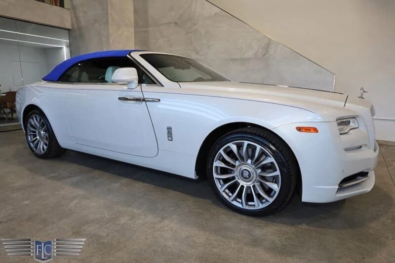 A white luxury convertible car with a blue soft top is parked indoors on a polished concrete floor near a staircase—an elegant example of exotic cars perfect for those seeking standout luxury.