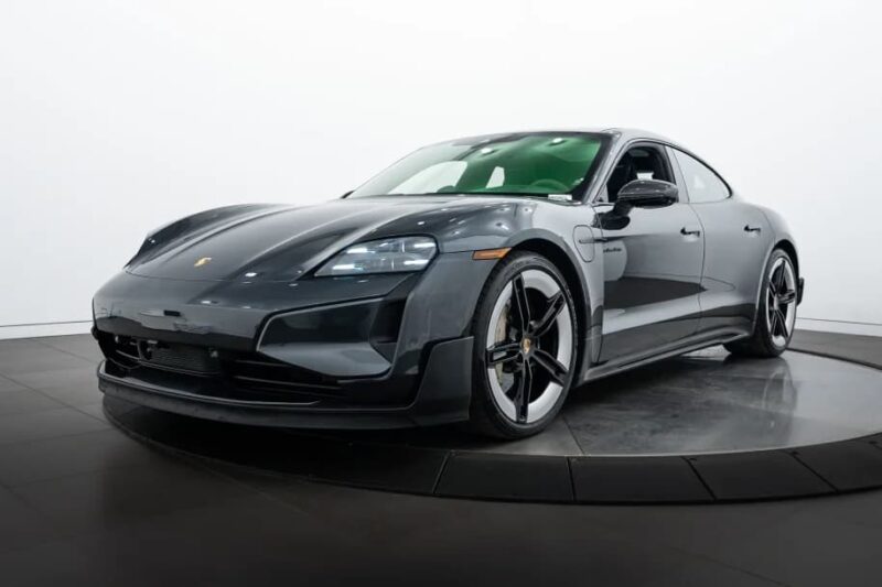 A black Porsche Taycan luxury car is displayed in a studio with a white background, positioned on a rotating platform.