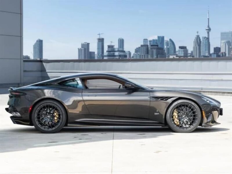 An Aston Martin DBS, the ultimate grand touring sports car, sits parked on a rooftop with a city skyline in the background.