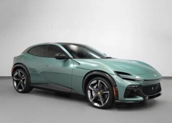 A metallic green Ferrari Purosangue SUV is parked in a plain indoor setting, viewed from the front left angle.